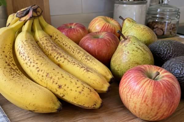 Bananes mûres posées près de pommes, poires et avocats sur un plan de travail