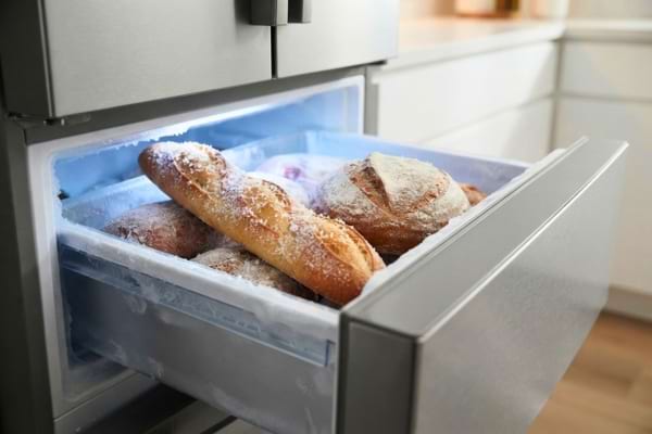 A slightly opened modern freezer drawer revealing a frozen French baguette