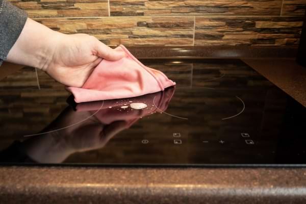 une personne passe un chiffon rose doux sur une plaque de cuisson à induction sale
