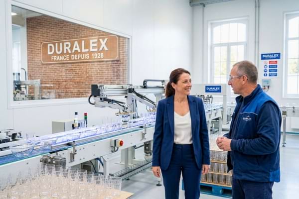 une femme d'affaires élégante et souriante en tenue décontractée chic, visitant une ligne de production de verre