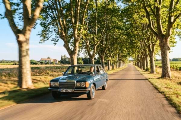 Une Mercedes 200 D vintage roulant doucement sur une magnifique route