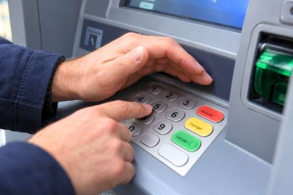 une main cachant soigneusement le clavier numérique d'un distributeur de billets