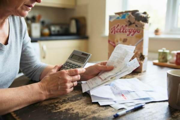 a person's hands holding a calculator and some bills on a kitchen table