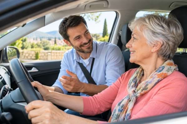 un moniteur d'auto-école souriant et rassurant, donnant des conseils à une conductrice senior