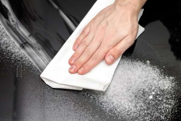 une personne passe un chiffon blanc sur une plaque de cuisson avec de la pâte de bicarbonate