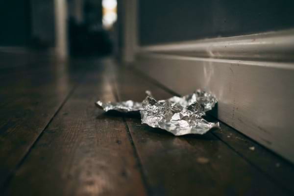 crumpled pieces of shiny aluminum foil placed on a wooden floor right next to a white wall baseboard