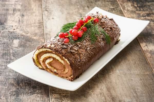 une bûche au chocolat roulée ans un plat blanc avec des décorations de Noël rouge