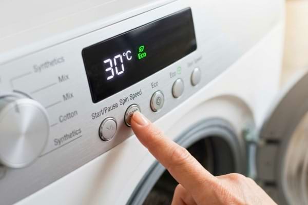 Un bandeau de commande de machine à laver moderne, avec un doigt appuyant sur le bouton "30°C"