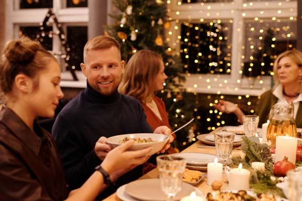 un homme passe un plat à une femme à une table décorée pour le réveillon de Noël en famille