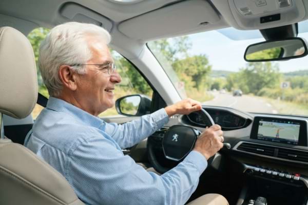 un homme senior aux cheveux blancs conduisant prudemment sa voiture en plein jour