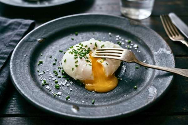 a perfectly cooked poached egg sitting on a rustic ceramic plate,