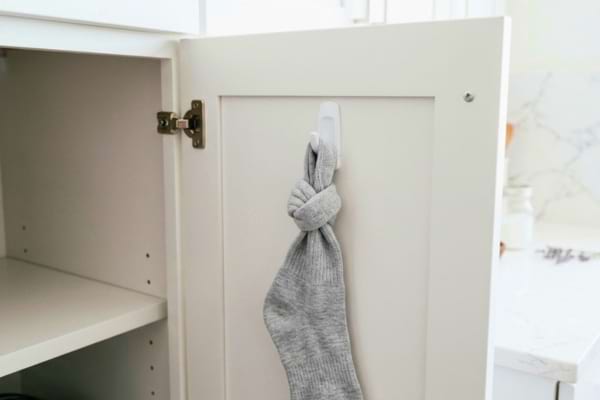 a clean grey sock tied with a tight knot at the top, hanging from a small white adhesive hook