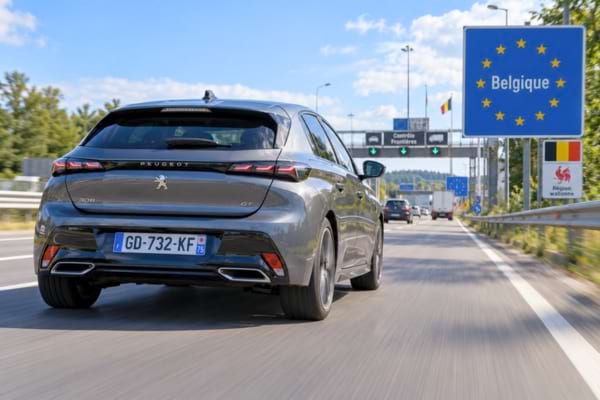 A French car with a visible 'F' on the blue license plate band, driving across the Belgian border on a highway