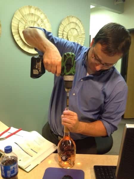 Un homme voulant dévisser sa bouteille en verre avec une perceuse