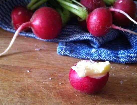 Radis avec du beurre sur une table en bois avec un torchon bleu.