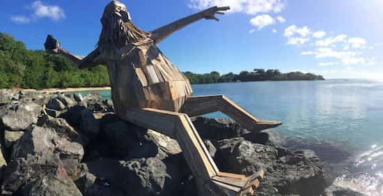 sculpture en bois d'un géant assis au bord de l'eau pour lancer une pierre