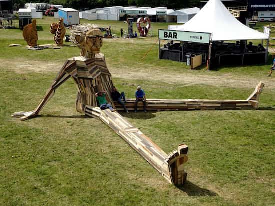 sculpture en bois recyclé d'un homme géant assis par terre